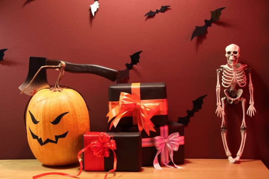 Cadeaux Halloween faits main noirs avec rubans rouges et roses, citrouille sculptée, squelette et chauves-souris sur mur bordeaux