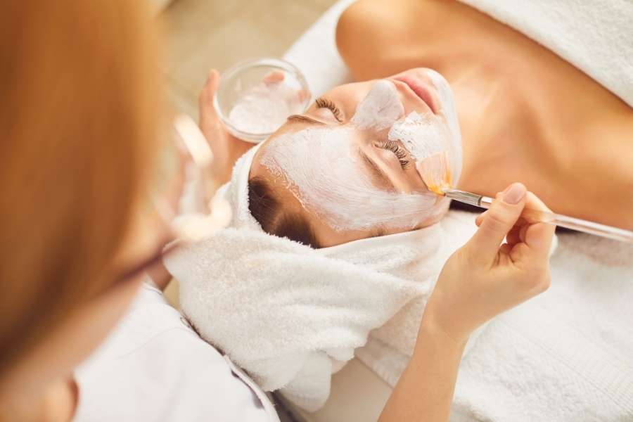 Esthéticienne appliquant un masque blanc sur le visage d'une cliente à l'aide d'un pinceau lors d'un soin en institut de beauté.